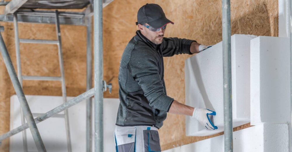 Isolierer auf einem Gerüst montiert weiße Dämmplatten an einer Wand.