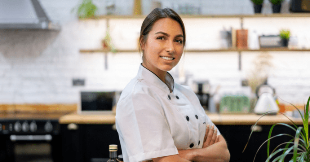 Mitarbeiterin steht in der Küche und lächelt in die Kamera